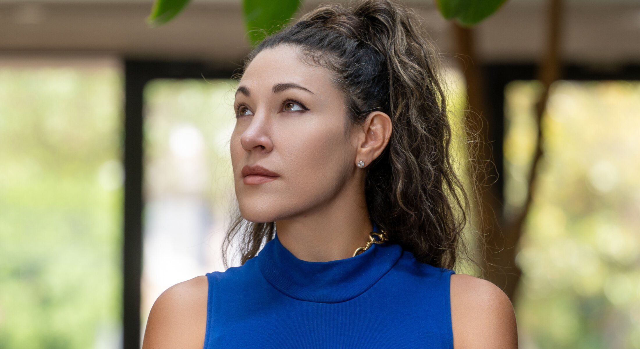 Woman in blue top looking up thoughtfully.