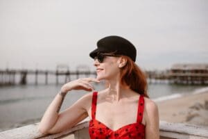 woman in sunglasses, hat, and red and polka dot dress, looking at the water