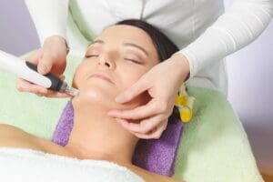Women with a yellow flower in her hair undergoing a microdermabrasion procedure, while laying her head on a purple towel.