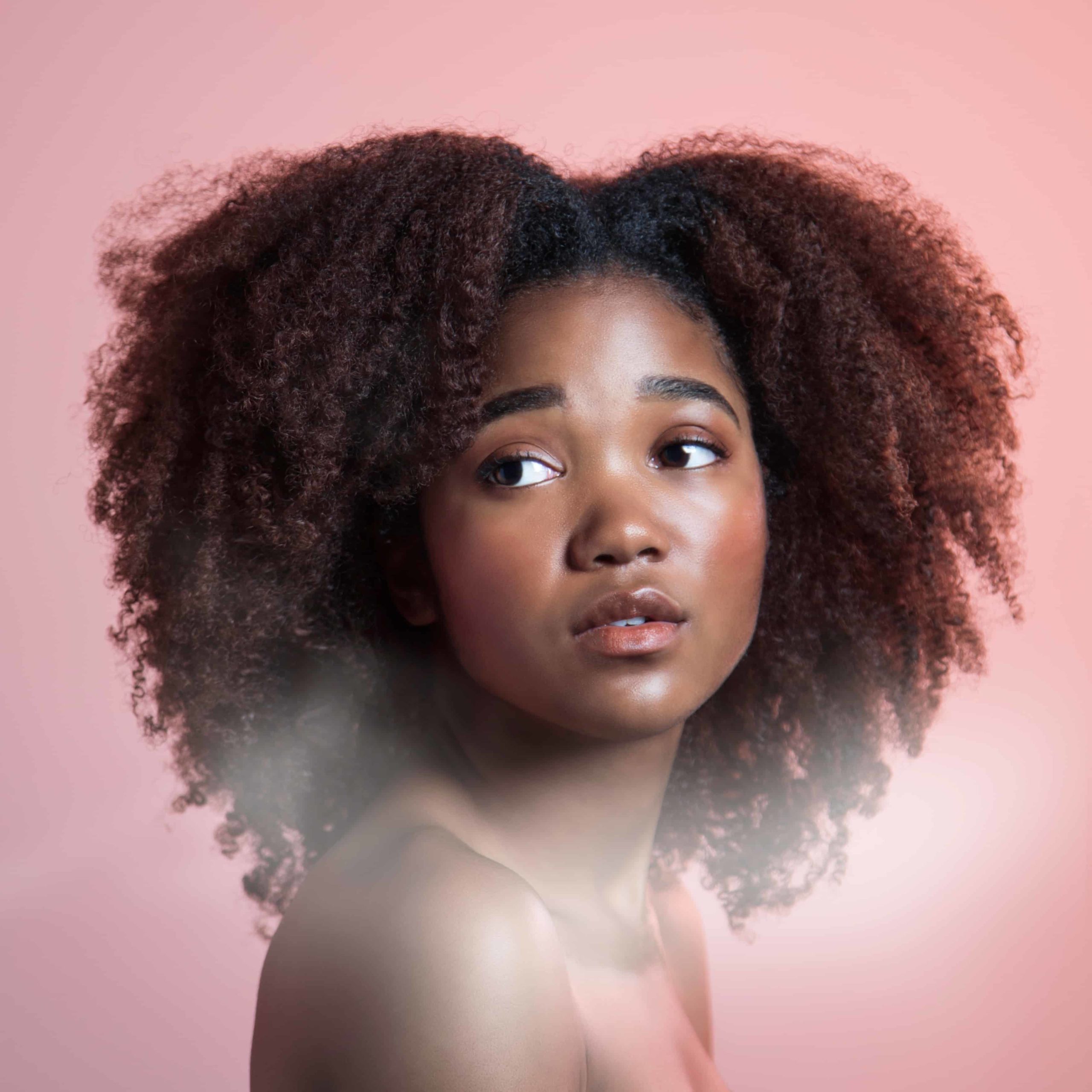 african american woman with natural curls looking at camera against a pink background