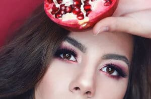 Close up portrait of woman's face holding up a pomegranate