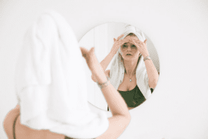 woman looking in mirror and putting lotion on her skin hair in towel