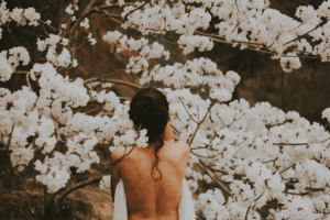 woman holding a towel to her chest looking toward blossoming trees, we see her back