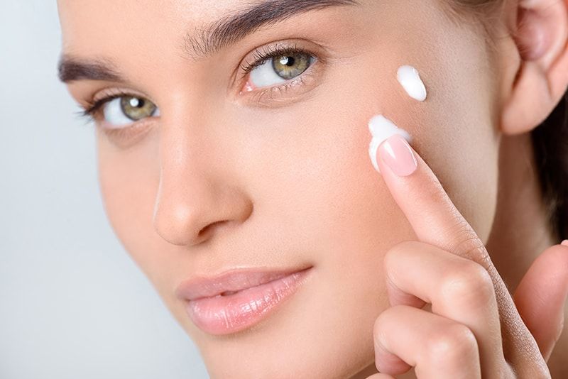 Close up portrait of woman's face applying skin cream with her finger