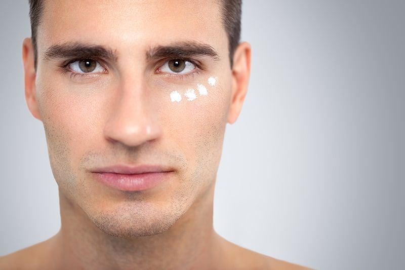 Face of handsome young man with moisturizer applied under his eyes.